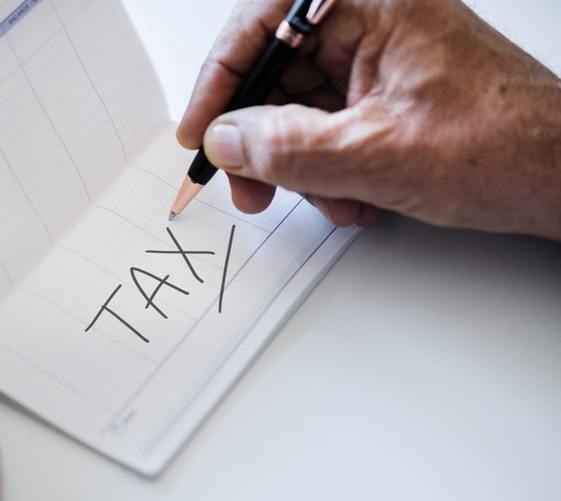 A man's hand writing the word 'tax' in a notepad with a pen